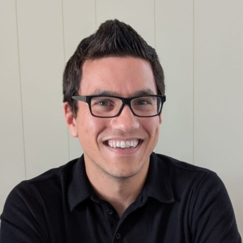 James Salamon James Salamon wearing black glasses and a black collared shirt, smiling in front of a light-colored paneled wall